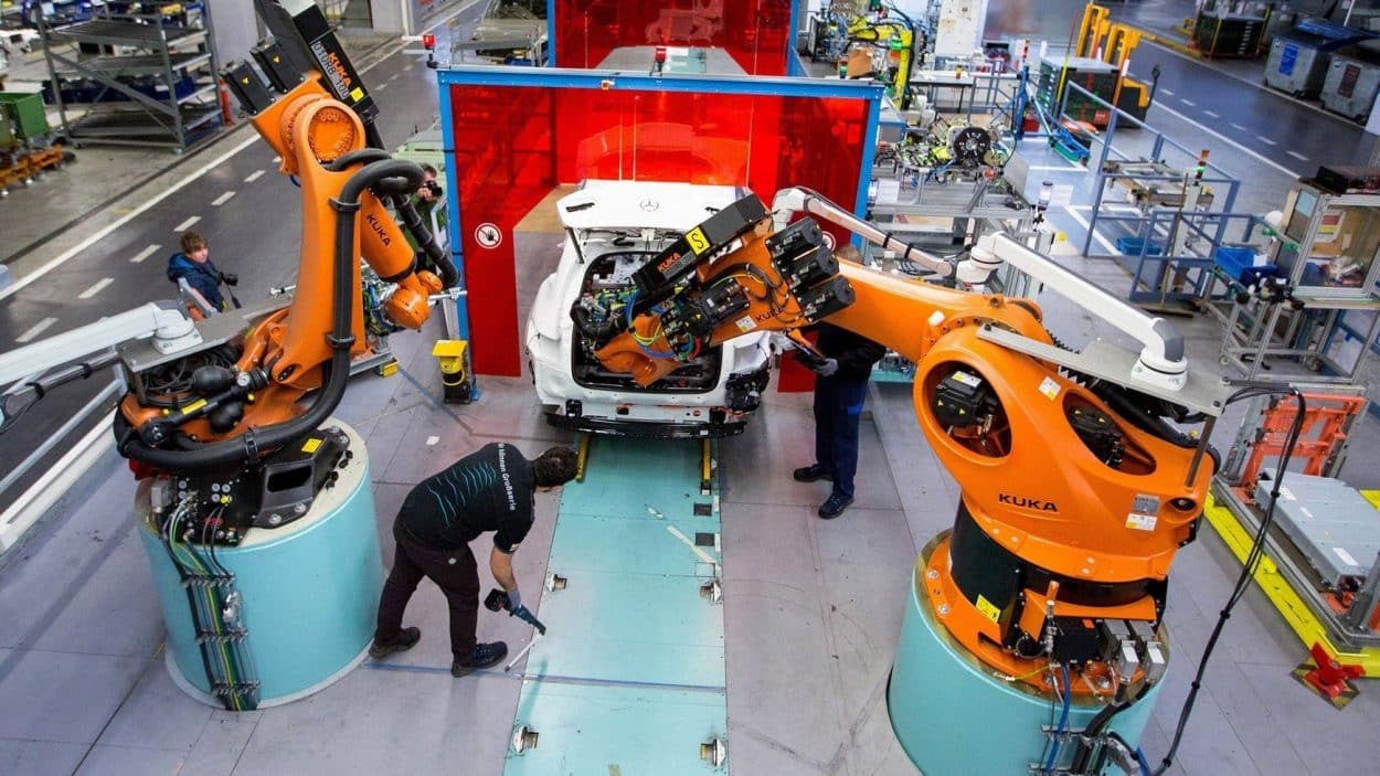 Employees work alongside robotic arms, manufactured by Kuka, at Mercedes-Benz's factory in Bremen, Germany © Bloomberg